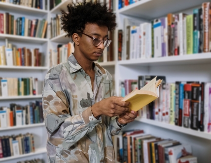 Teen reading book in front of book shelves