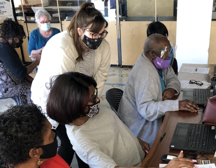 woman stands helping others on laptops