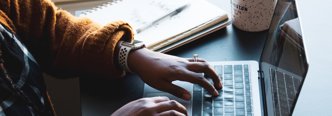 person typing on laptop next to coffee mug and notebook with pen