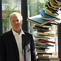 man stands by sculpture made of books
